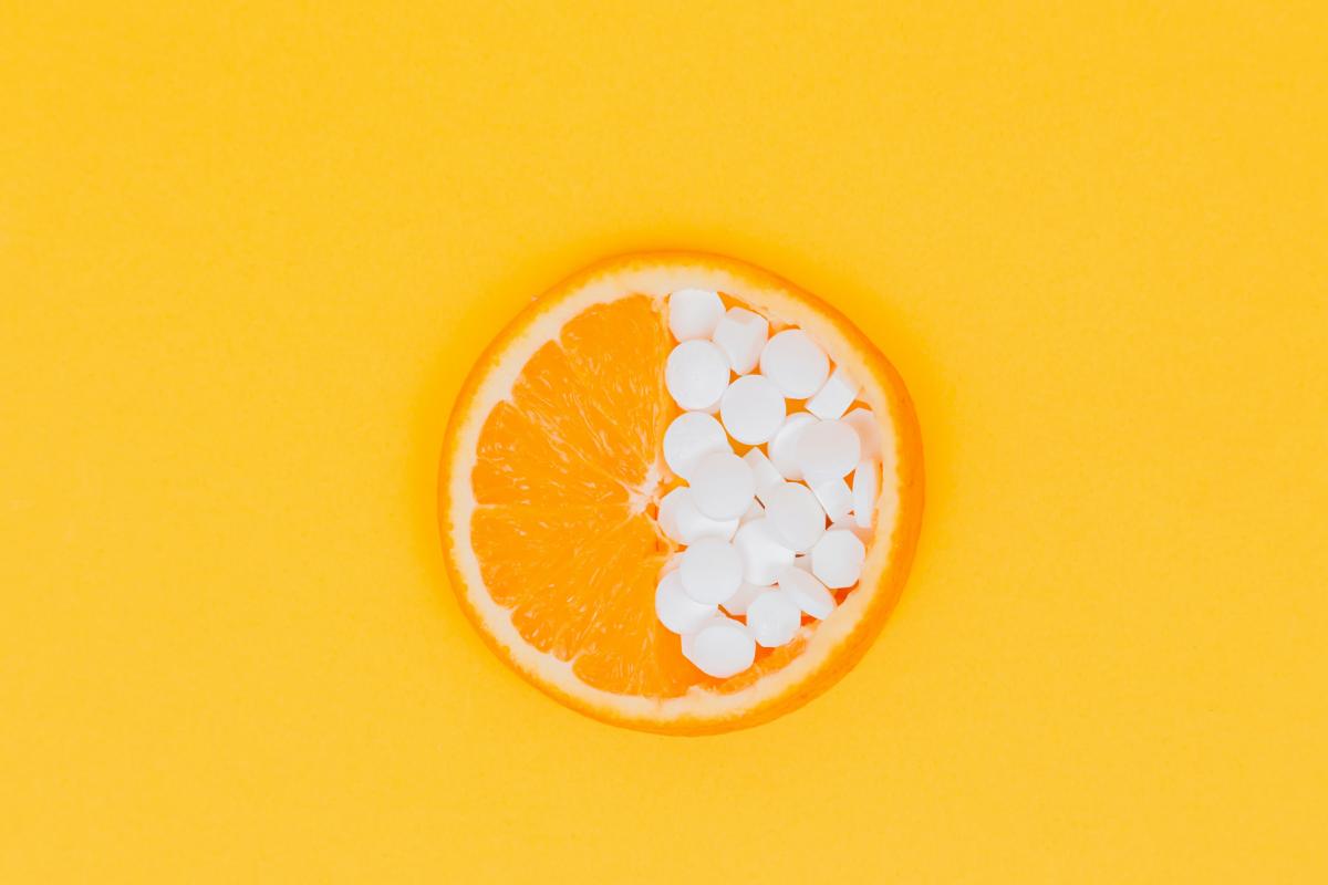 A photo of an orange cut up in the middle. The right side of the orange is filled with white round tablets. 