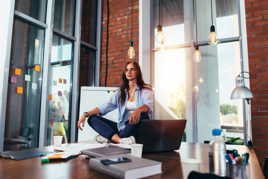 A woman performing peacefull meditation pose at her workplace