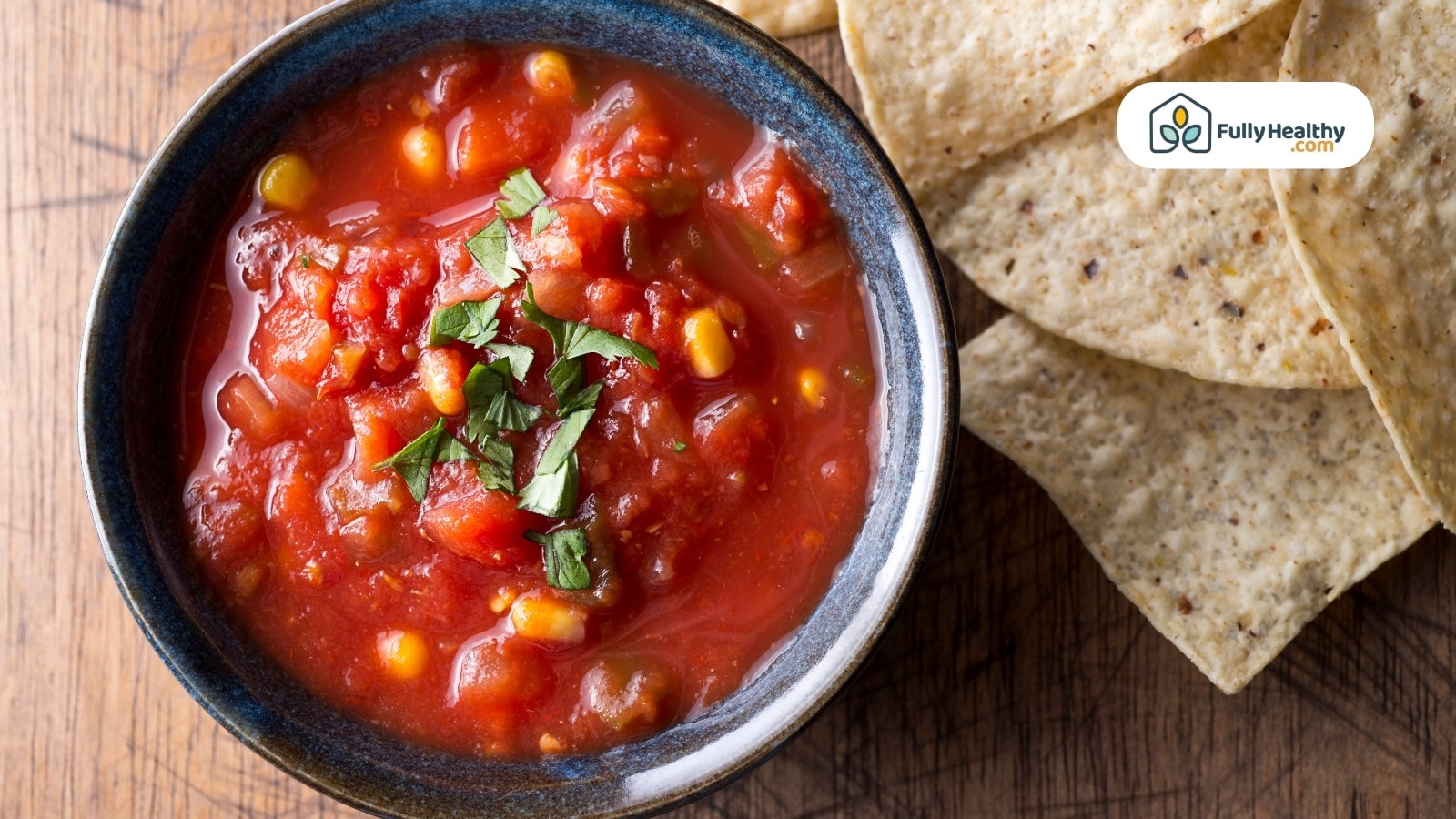 Bowl of chunky tomato salsa with tortilla chips on wooden table