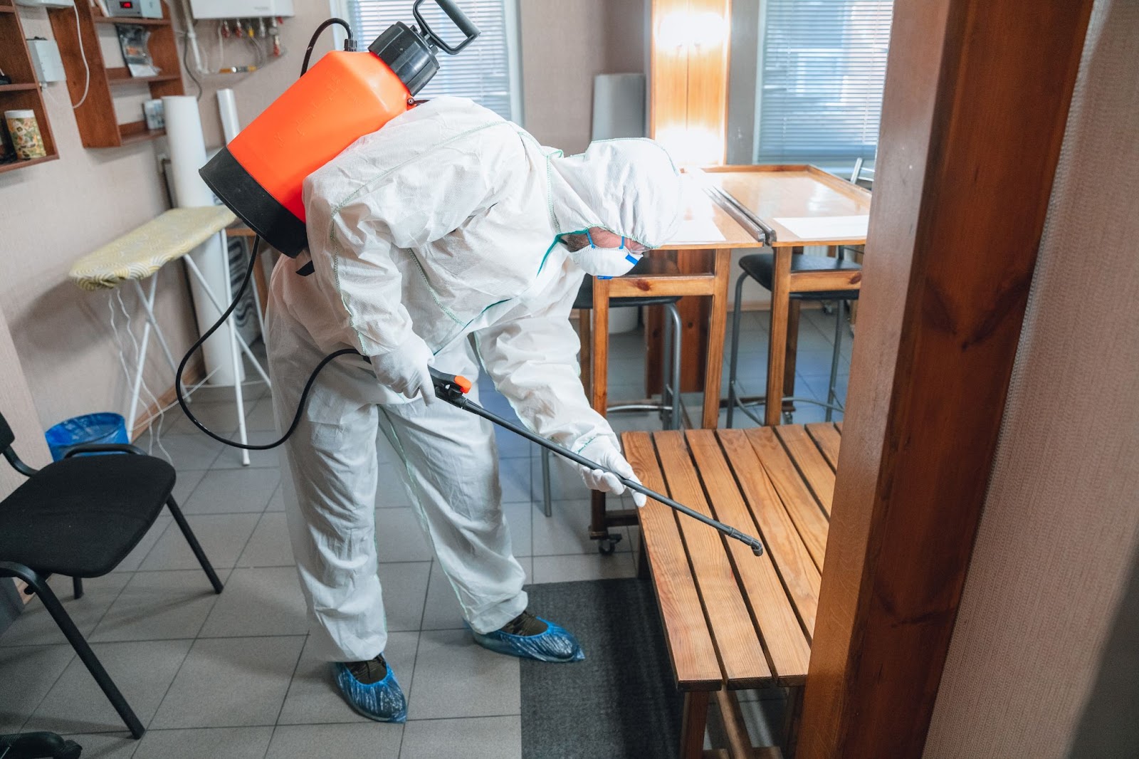 Pest control professional spraying indoors in full protective gear