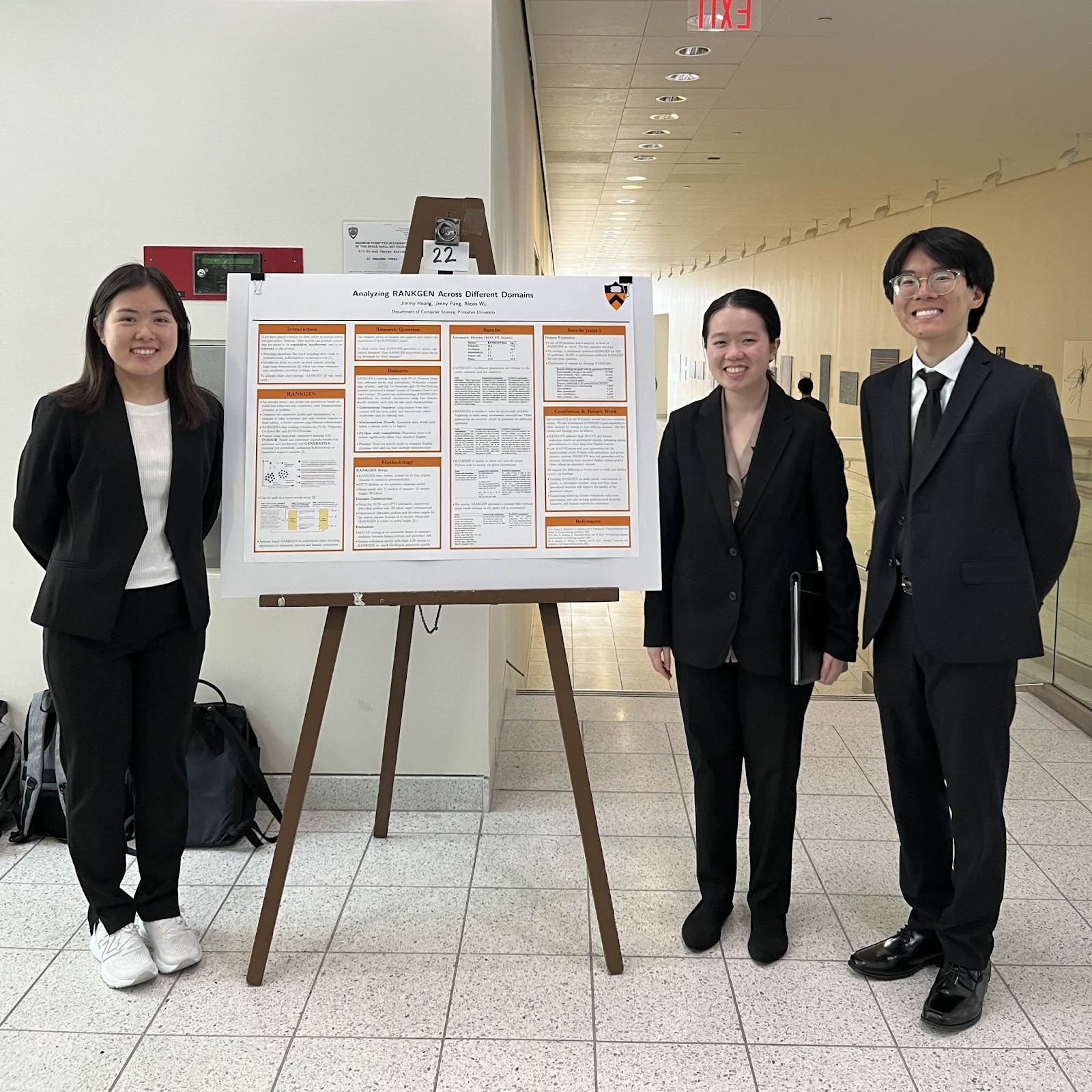 Photo of three students wearing black suits and smiling at the camera. Machine learning research poster in the center.