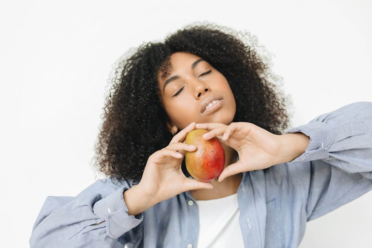 A woman with curly hair holds an apple, symbolizing the connection between diet and hair and scalp health.