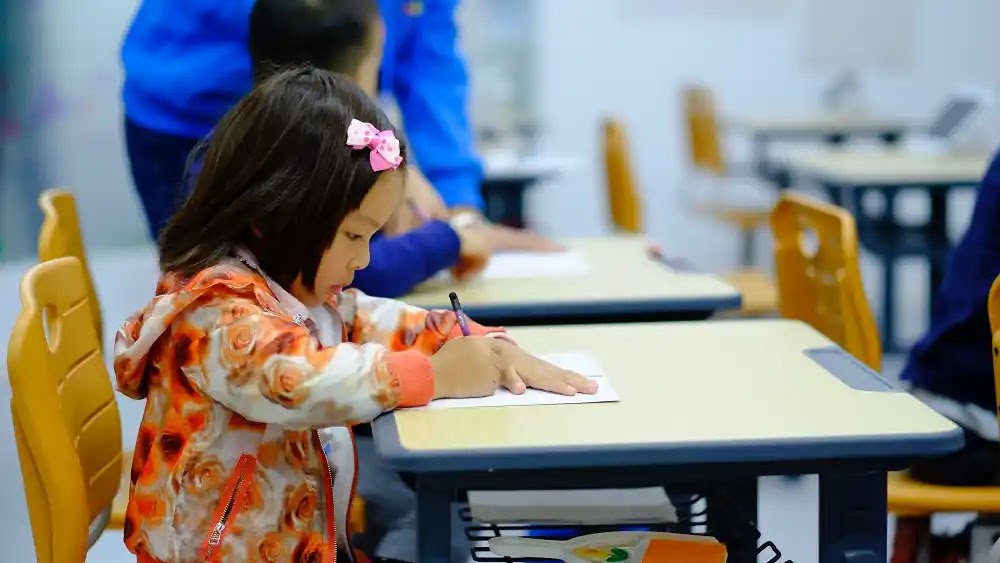 seorang anak kecil sedang menulis di ruang kelas