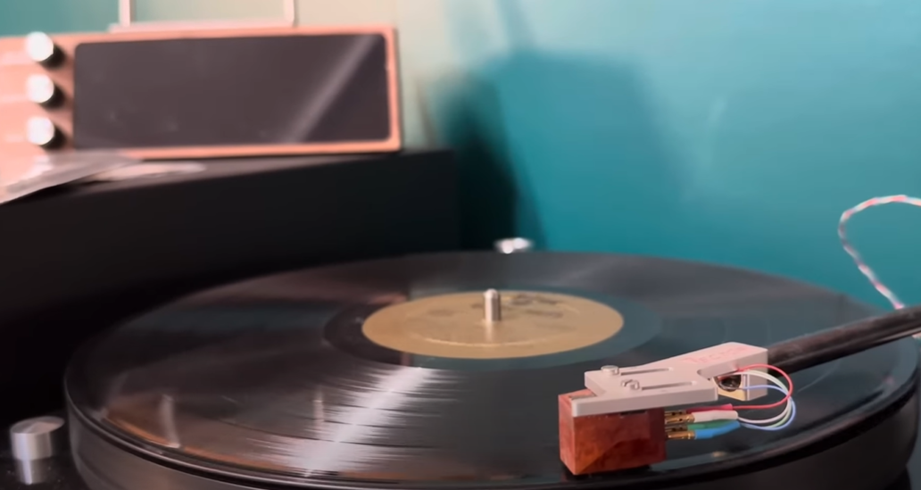 A vinyl record playing on a turntable with a connected tonearm and cartridge. 