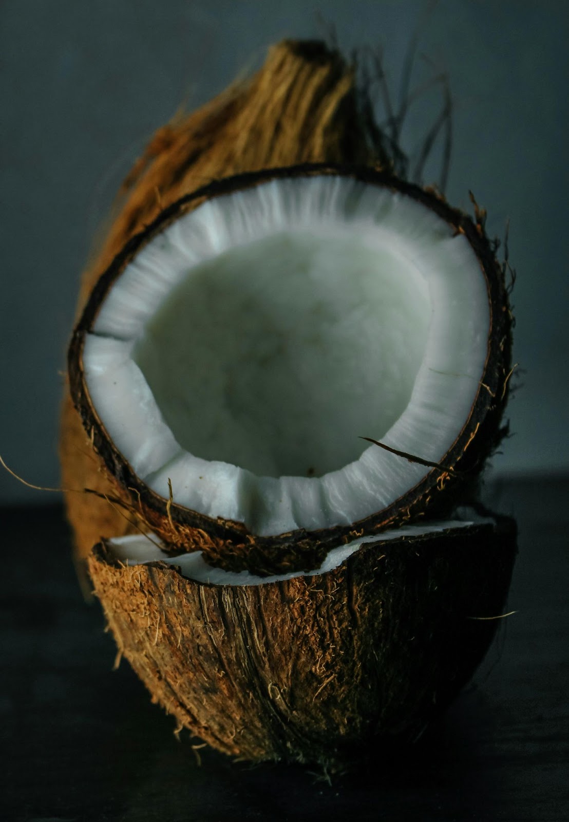 Close up moody imag of a coconut that has been freshly cut open exposing the white skin. Featured in the blog "Can I Use Coconut Oil As A Body Cream?"