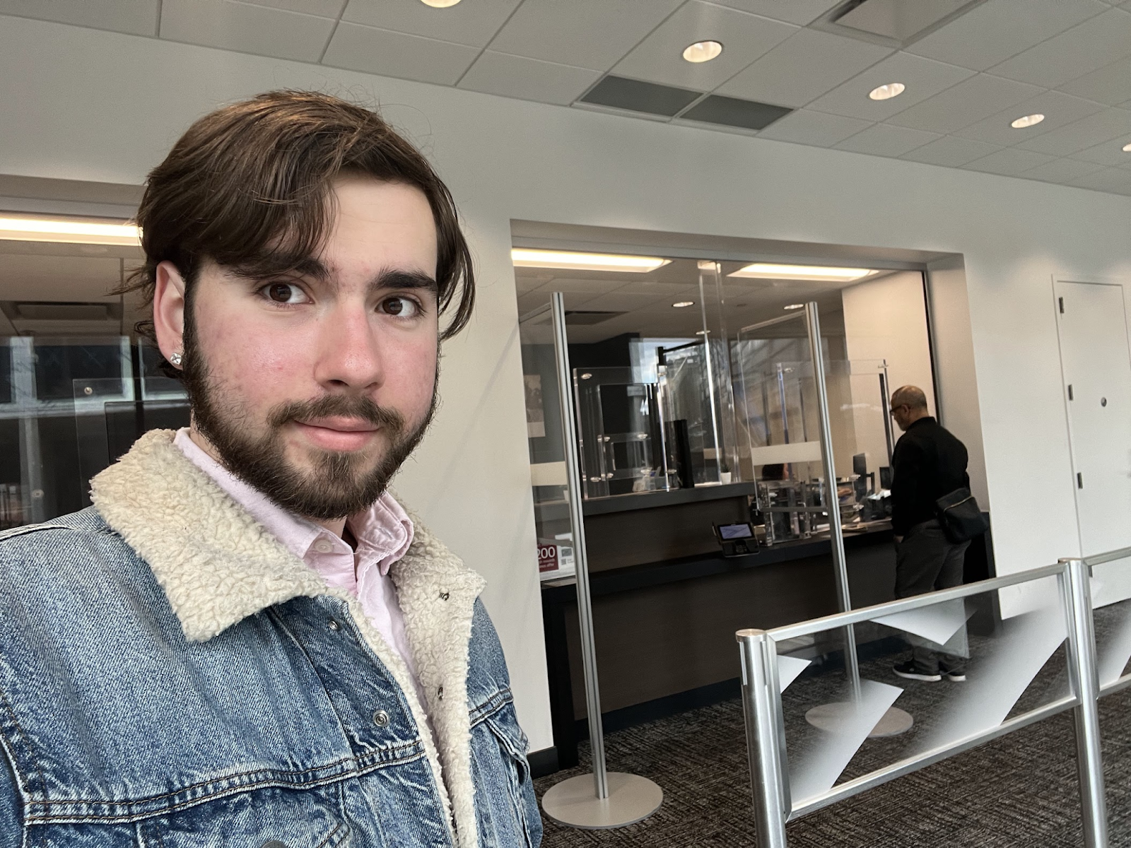 Research assistant Sammy, a young man, in front of thick glass at a teller window.