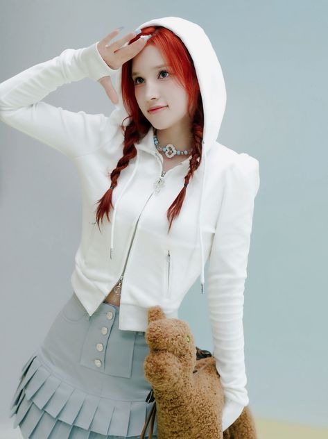 This may contain: a young woman with red hair wearing a white hoodie and blue skirt holding a teddy bear