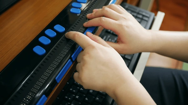 A visually impaired individual using a Braille for computer keyboard with tactile buttons and assistive technology