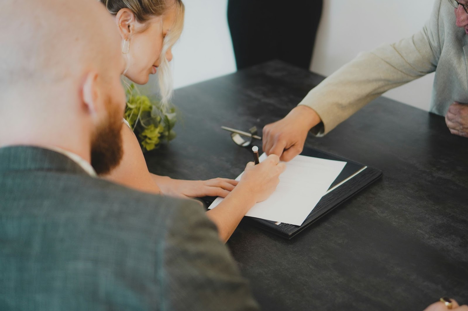 Two persons and an elderly man at a desk, discussing and signing important documents