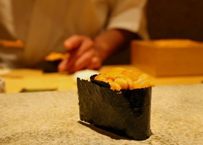 Fresh uni sea urchin gunkan sushi; a chef is preparing more sushi in the background.