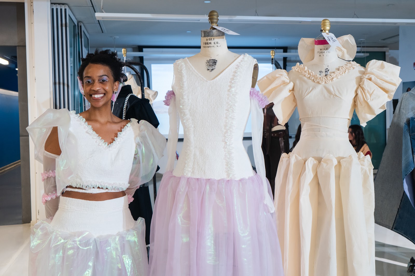 Camillia Zachary standing next to her design creations showcased on mannequins. 