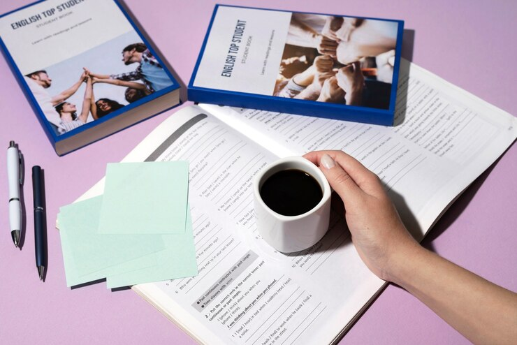 English book resting on the table of working space with a hand holding a coffee mug on top