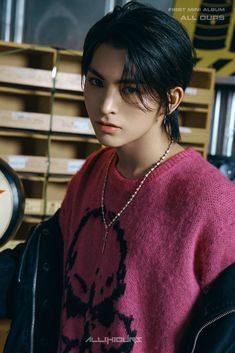 This contains an image of Masami  with black hair wearing a pink sweater and necklace standing in front of wooden shelves