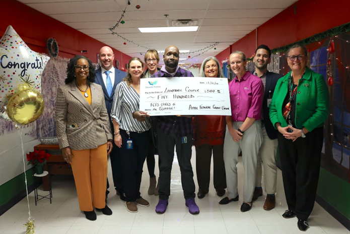 Group of people surrounding Lawrence Cooper, who is holding up a large $500 check for being honored by FCPS Cares. 