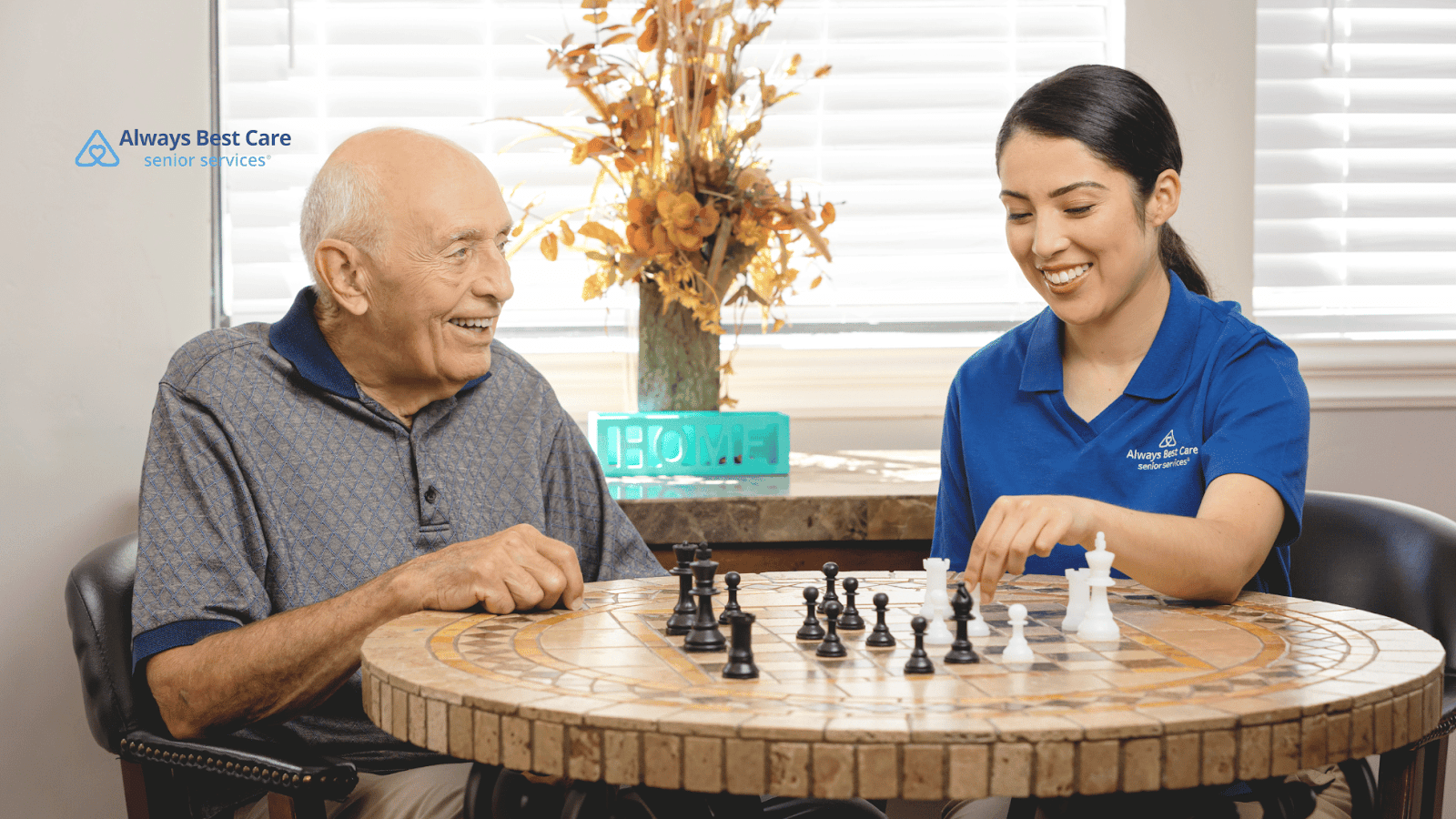 This image depicts a senior man playing chess with a caregiver