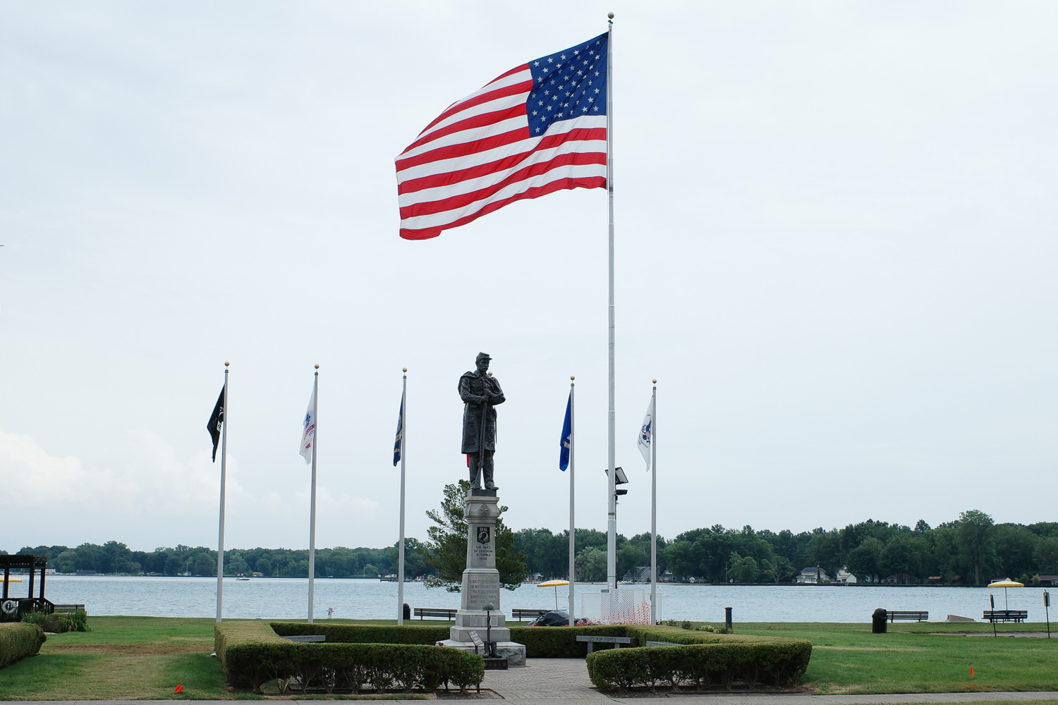 American flag and memorial flags next to statue of civil war soldier with POW-MIA logo in park in Algonac.