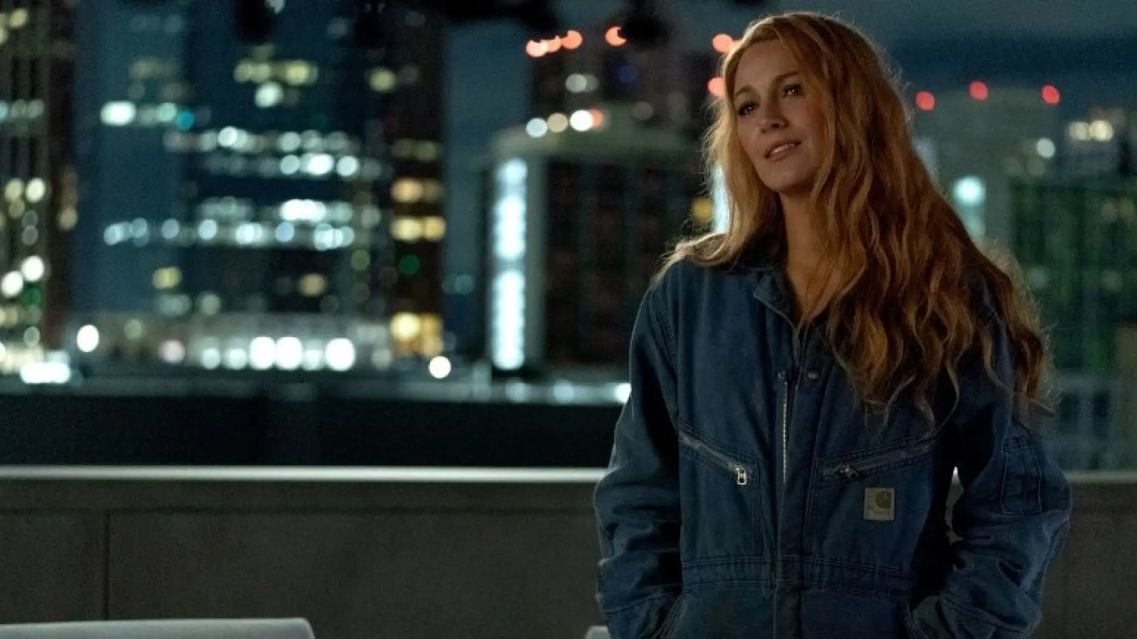 Blake Lively con chaqueta de mezclilla en una escena nocturna con la ciudad iluminada al fondo en Romper el Círculo.