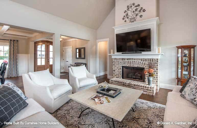 Great room with beige seats, a wooden coffee table, and a brick firepGreat room with beige seats, a wooden coffee table, and a brick fireplace topped with a TV.lace topped with a TV.
