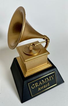 This contains an image of gramy award on a black and gold pedestal with a white background