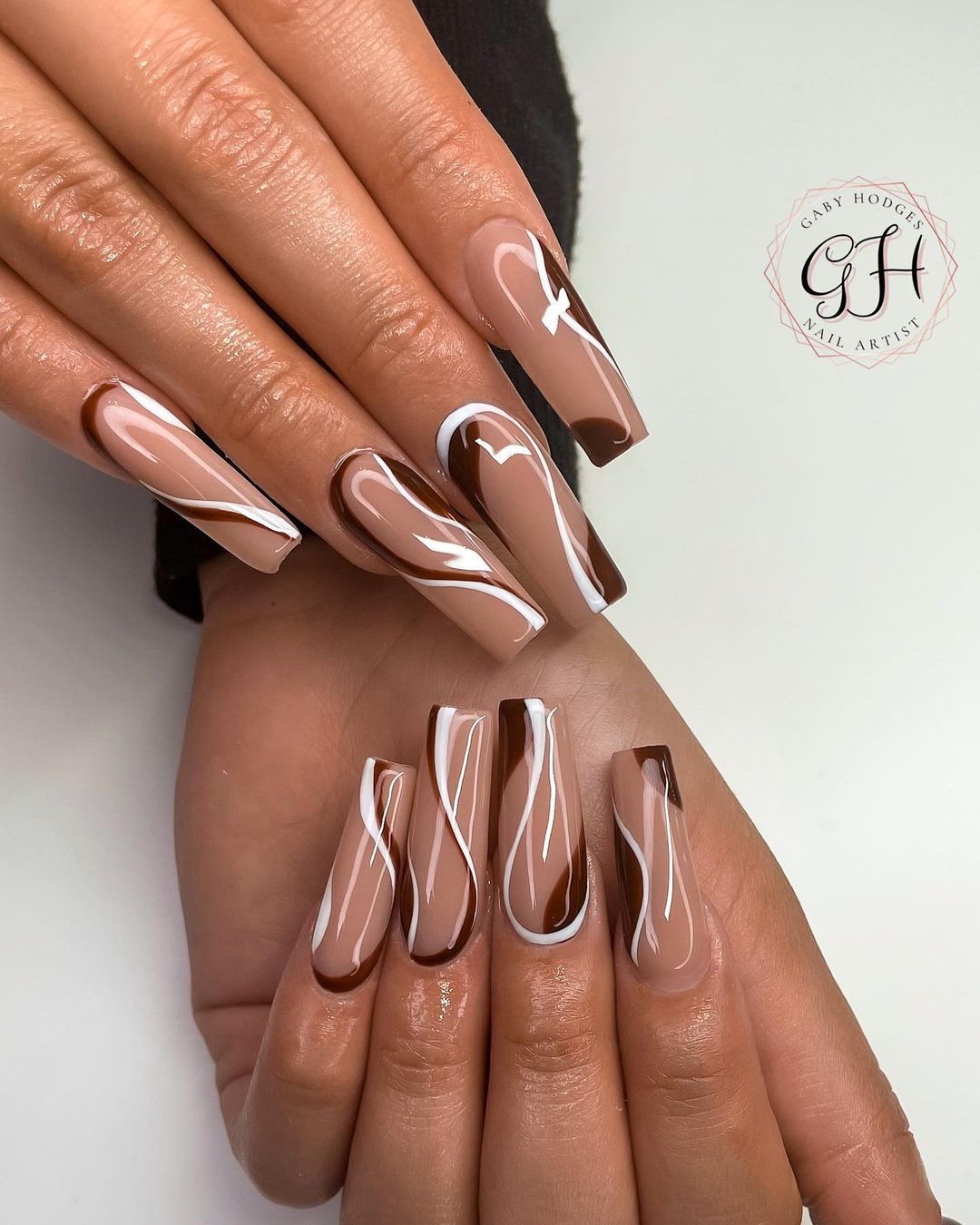 Long, glossy nails with brown and white swirl nail art, displayed on a hand against a light background.

