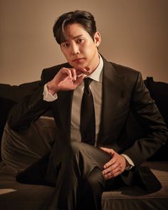 This contain: a picture of  Park Sung Hoon in a suit and tie sitting on a couch with his hand under his chin