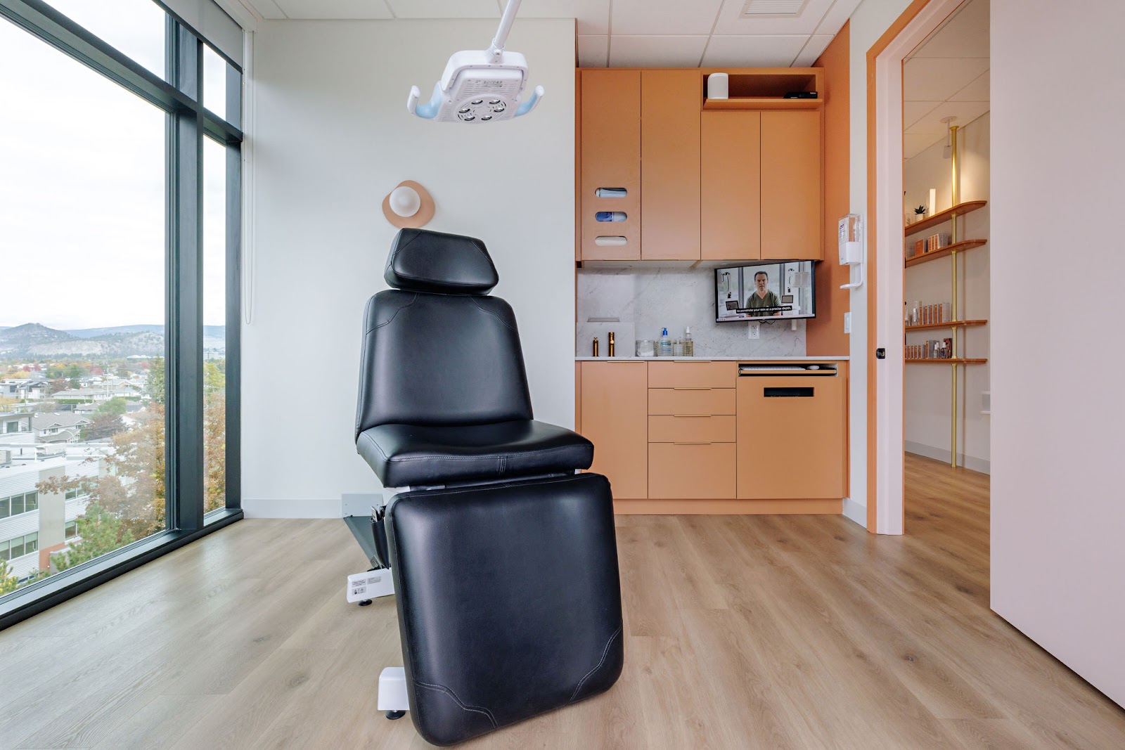 An examination room in Dr Ben Wiese's office with wooden floors, light walls, a patient chair in the middle, and a big window on the left with a view of Kelowna.