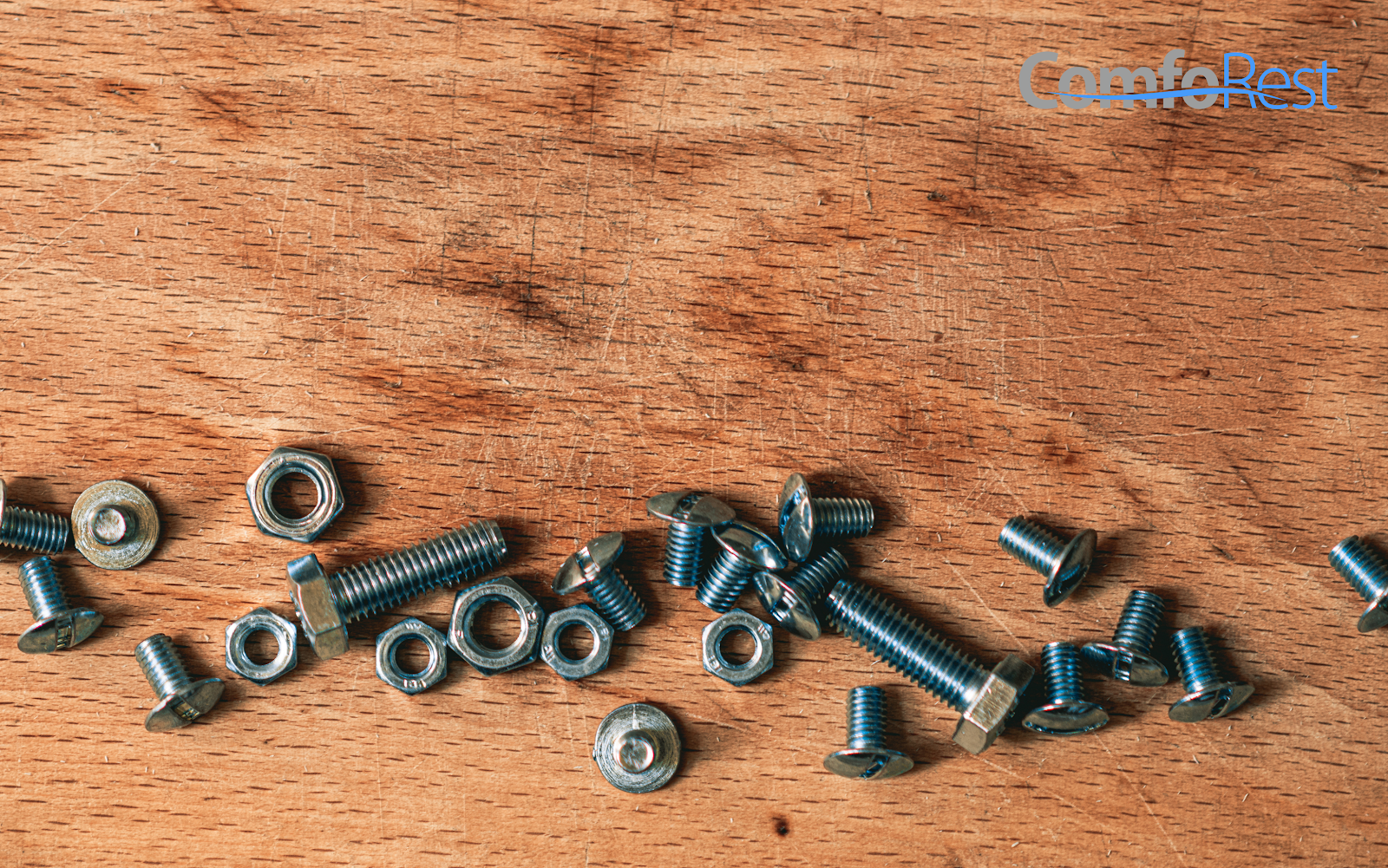 Scattered metal screws and nuts on a wooden surface.