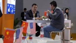 资料照:在上海举行的中国国际进口博览会期间,参观者在美国一家推广环境传感器公司的展位上在摆放着美中两国国旗的桌边谈话。(2019年11月6日)