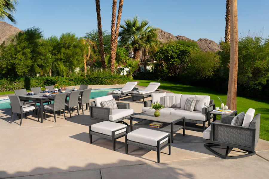 A luxurious outdoor seating and dining setup featuring multiple Sunbrella® furniture pieces, including lounge chairs, dining chairs, and a sectional, placed beside a sparkling pool with palm trees and mountain views in the background.