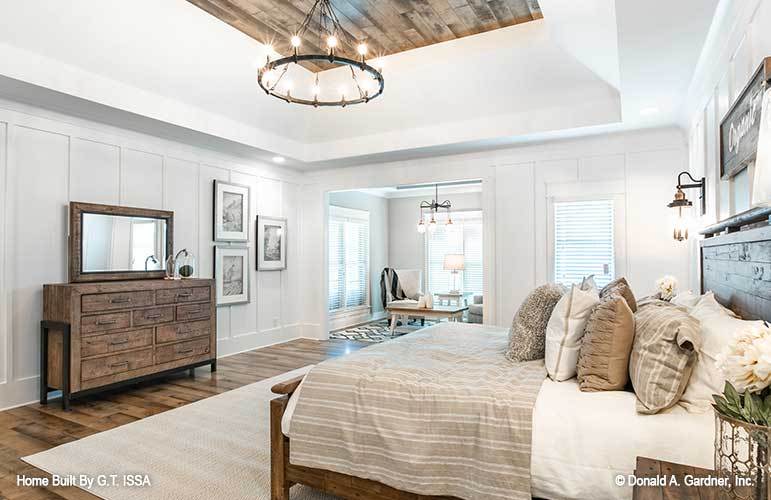 A stunning coved ceiling adorned with wood planks and round chandelier crowns the primary bedroom.