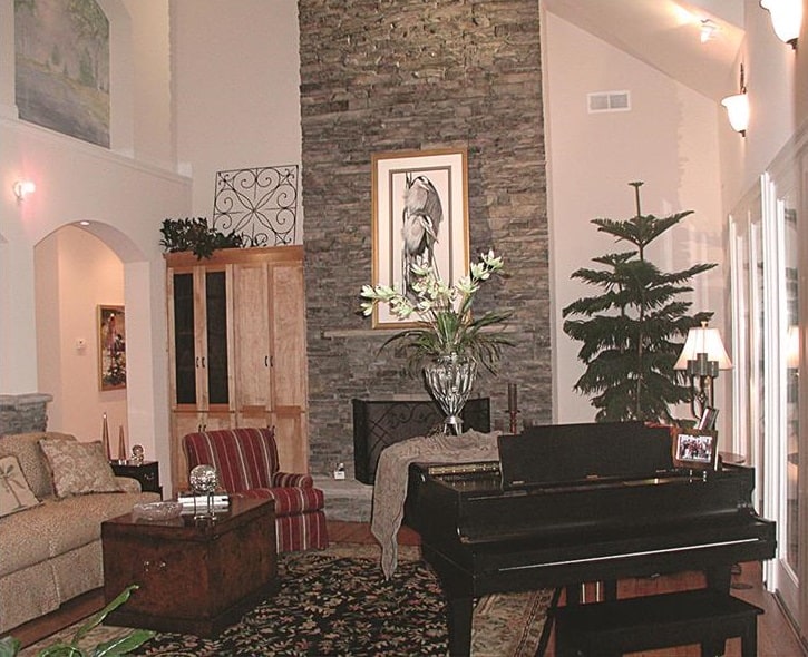Family room with skirted seats, a baby grand piano, and a stone fireplace adorned with a framed artwork.