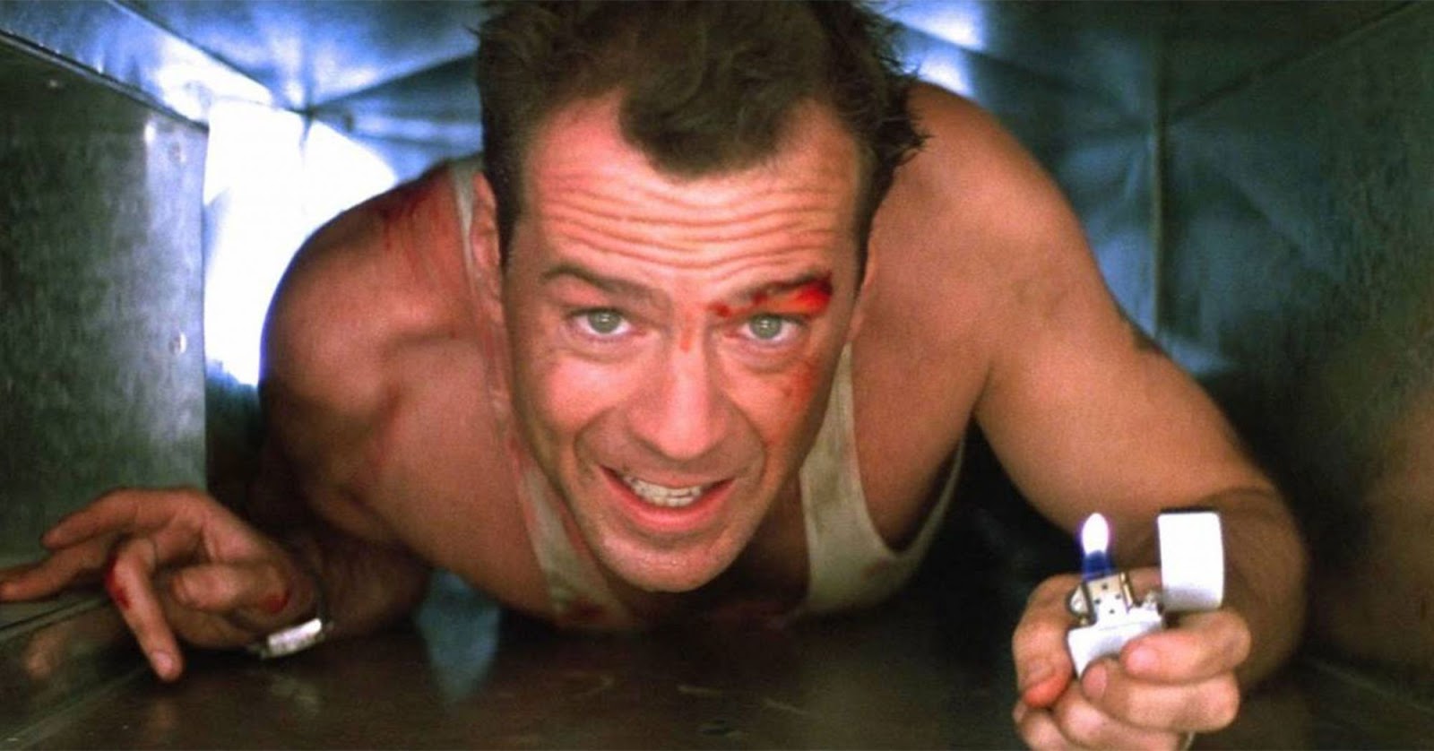 John McClane herido en un ducto de ventilación sosteniendo un encendedor con expresión de tensión en el hotel Nakatomi Plaza.