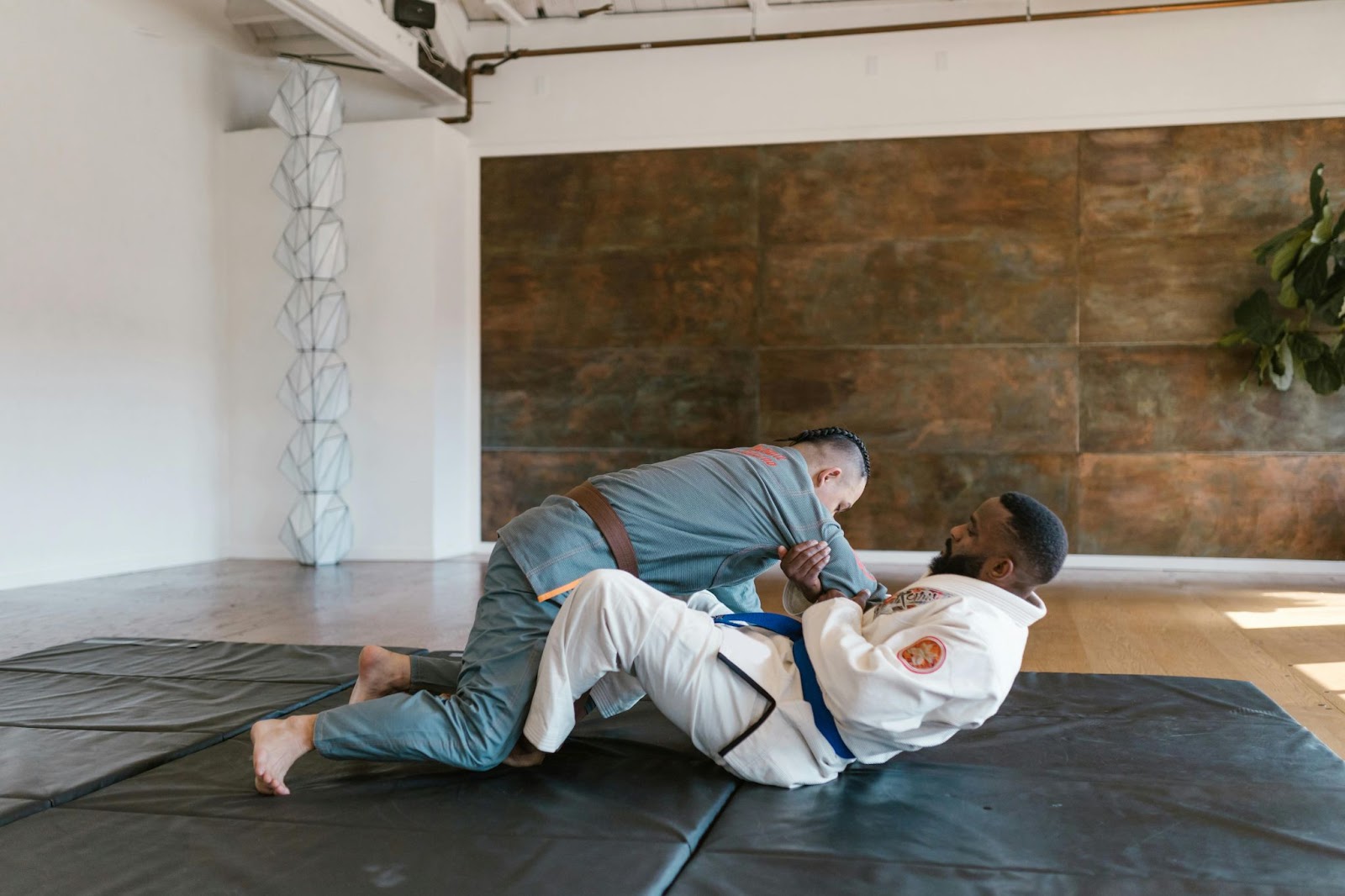 A martial arts instructor pulls a student's arm while grappling on the floor, demonstrating a technique.