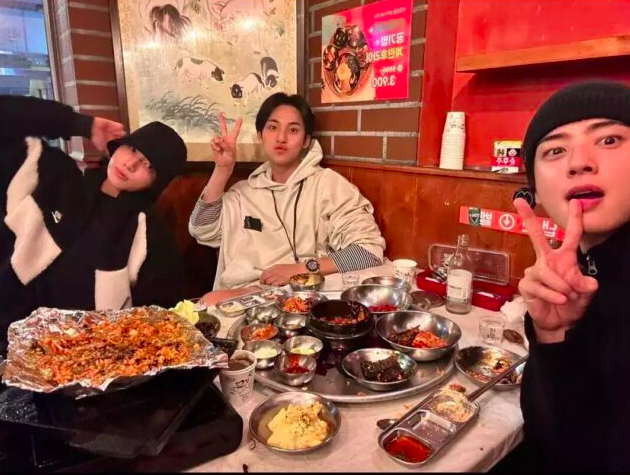 This contains an image of Jungkook, and Mingyu, with  DK from SEVENTEEN sitting next to each other at a table with food and drinks on it