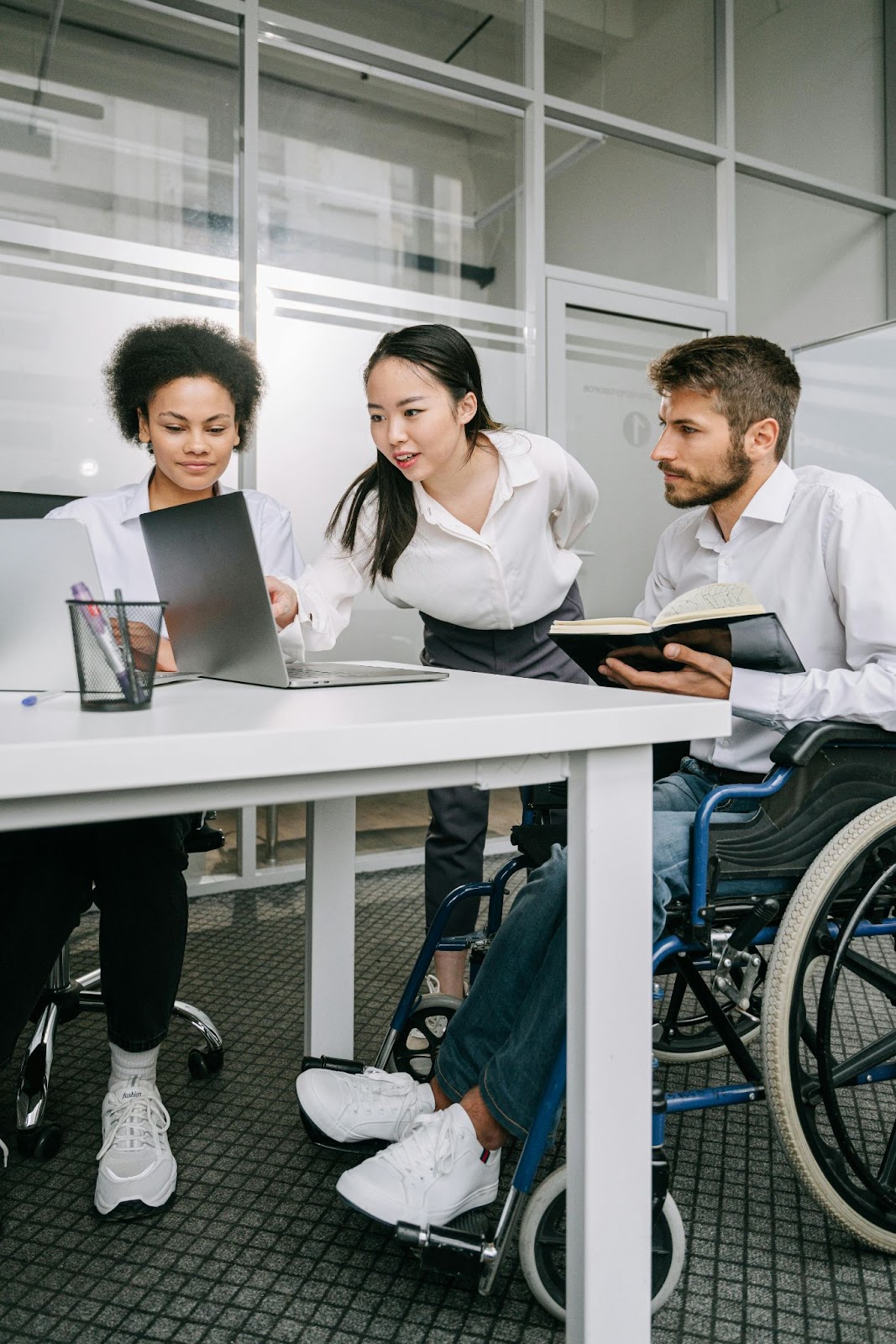 Three office workers look at a laptop on a table.