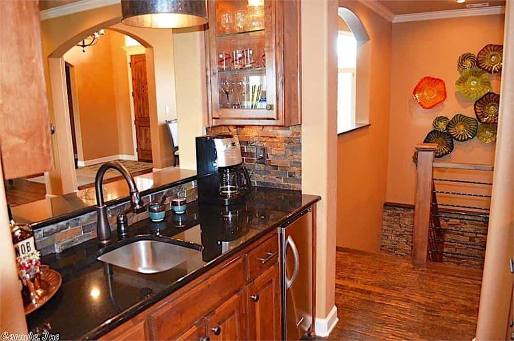 The wet bar is equipped with a sink, wooden cabinets, a granite countertop, and a raised serving bar.