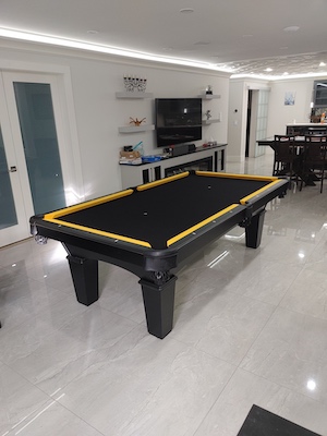 Black felt pool table with yellow bumpers in a basement with white floors.