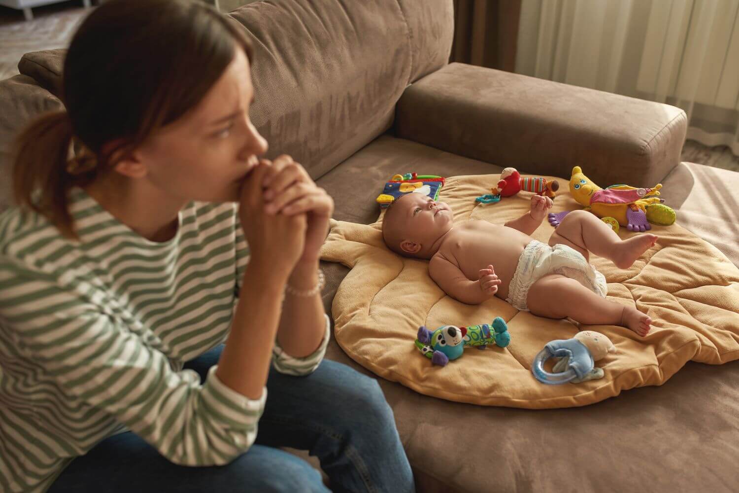 stressed woman sitting next to a baby on a play mat