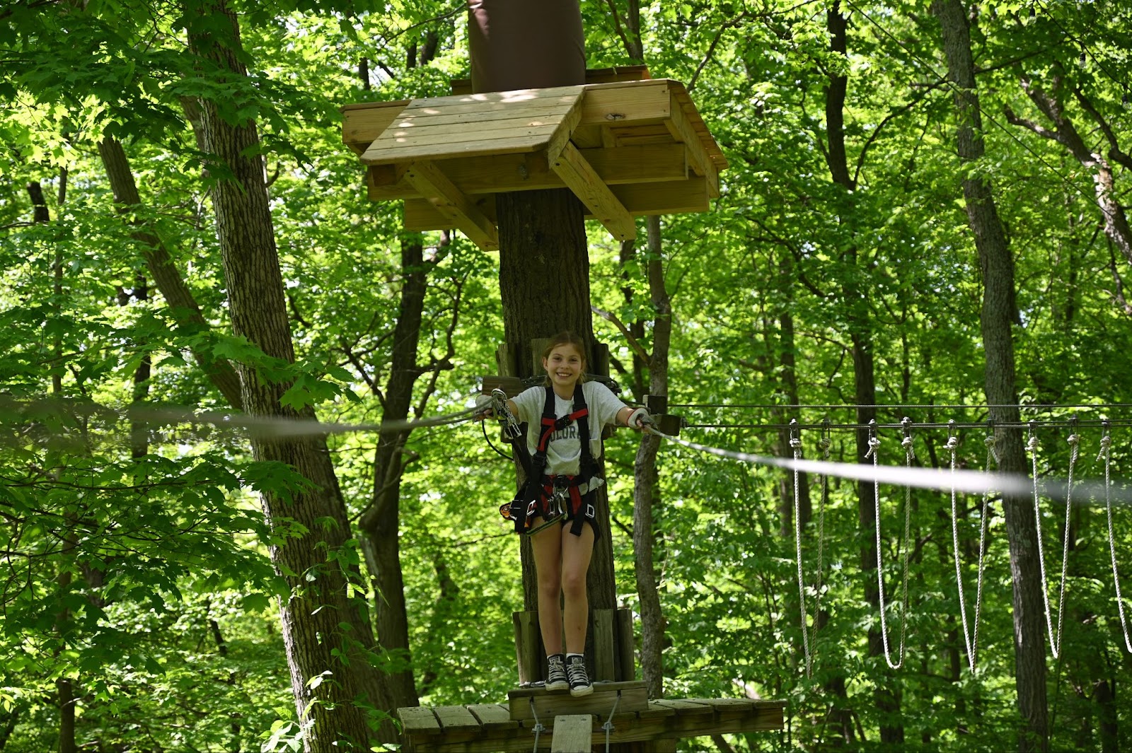 Young girl wearing safety gear, standing on a platform and ready to zip line at TreEscape Aerial Adventure Park in Vernon, NJ.