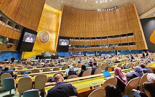 This contain an image of  people sitting at tables in a large room with many screens on the walls and ceiling