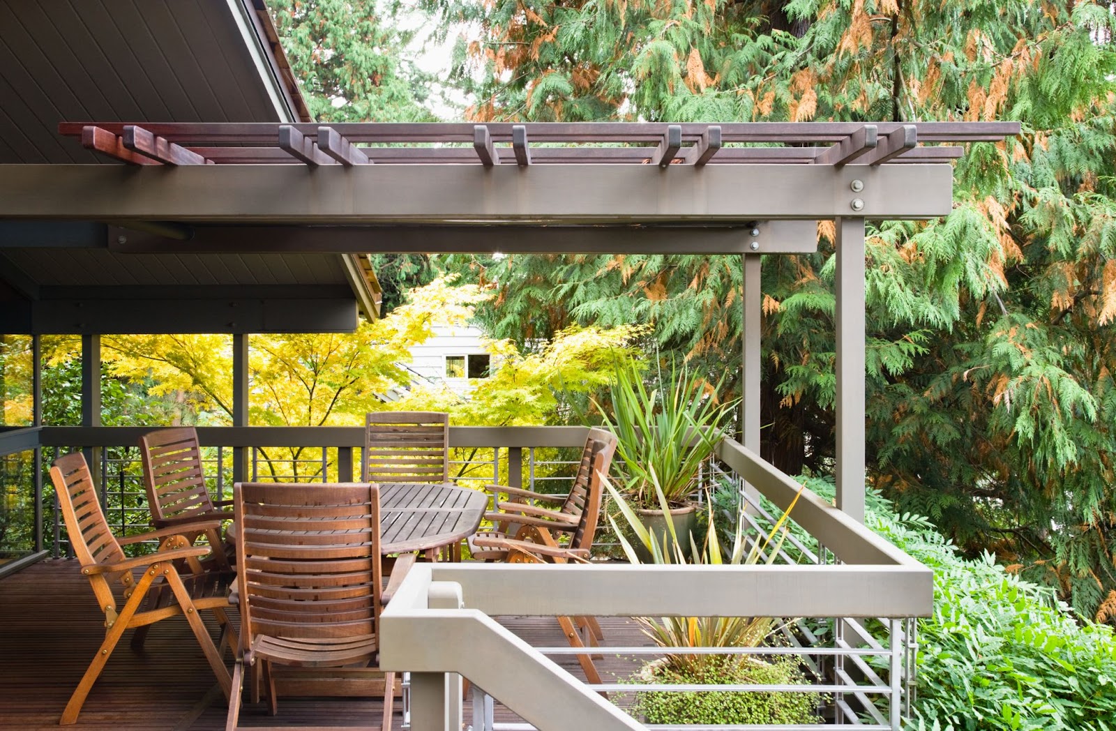 Chairs and a table on a raised custom wooden deck with an awning, surrounded by railings and plants.