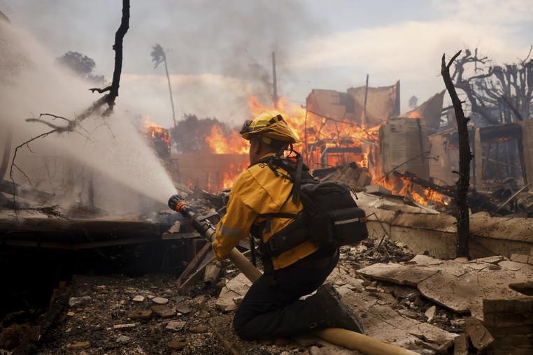 A firefighter battles the Palisades Fire around a burned structure in the Pacific Palisades neighborhood.