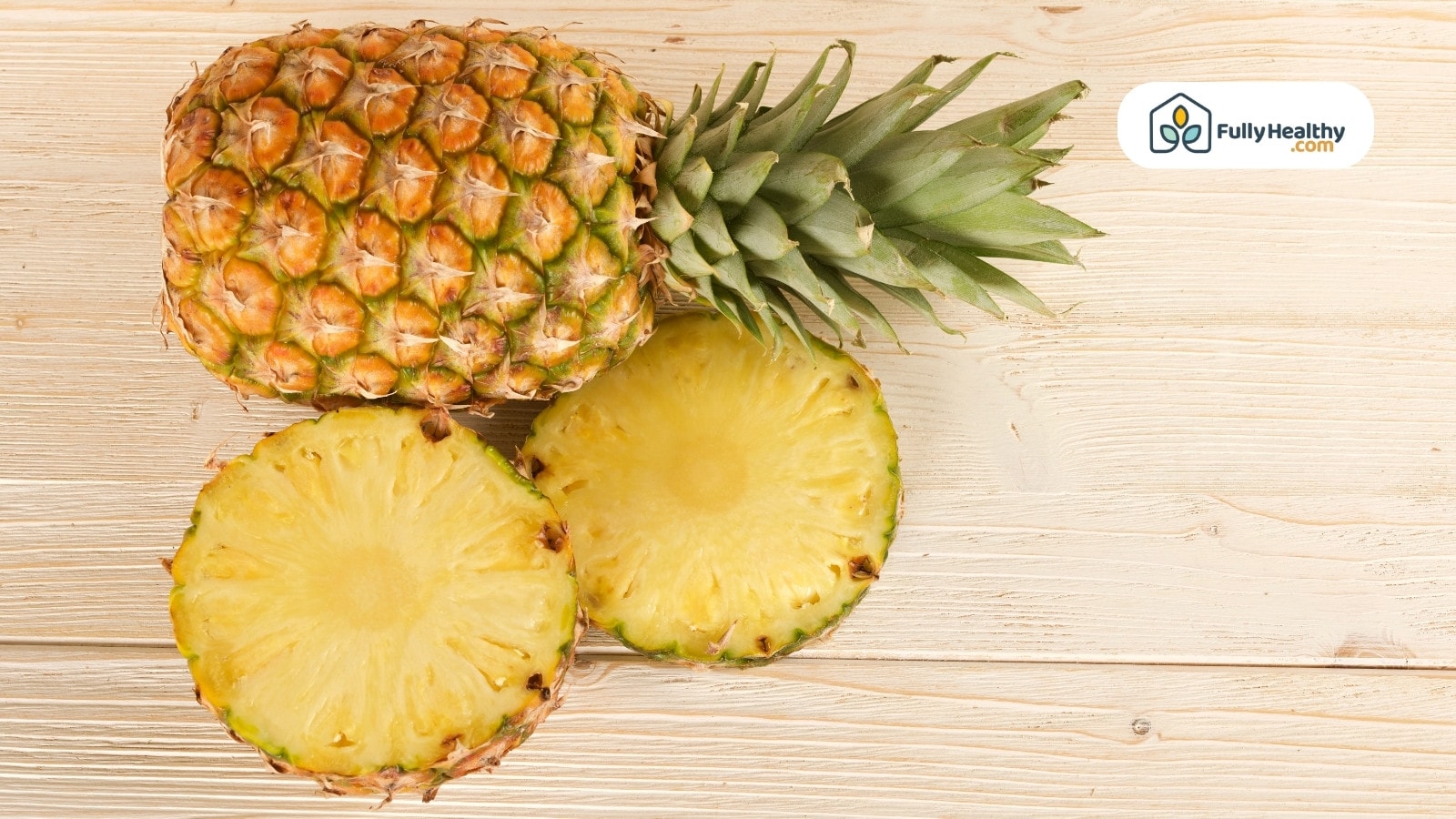 Whole pineapple and two slices resting on light wooden background