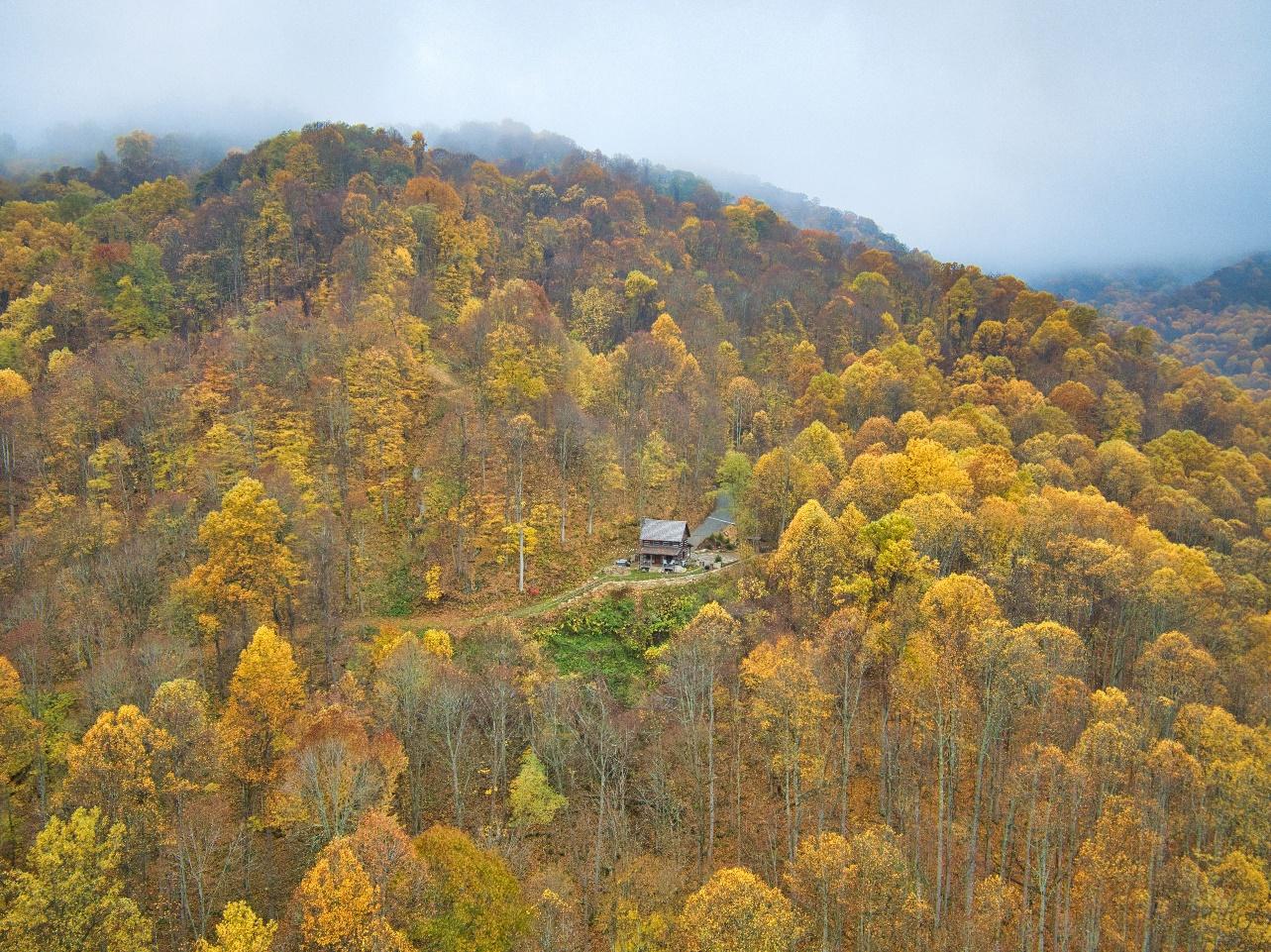 Aerial view of The Cabin and the diverse terrain at The Retreats at Spring Creek Preserve featuring ridges, expansive mountain views, streams, waterfalls, and forested areas.
