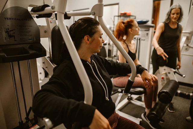 Women working out together in a gym, using a weight machine for strength training.