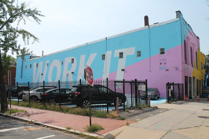 The exterior of a building with a blue, pink, and white mural that says Work It. 