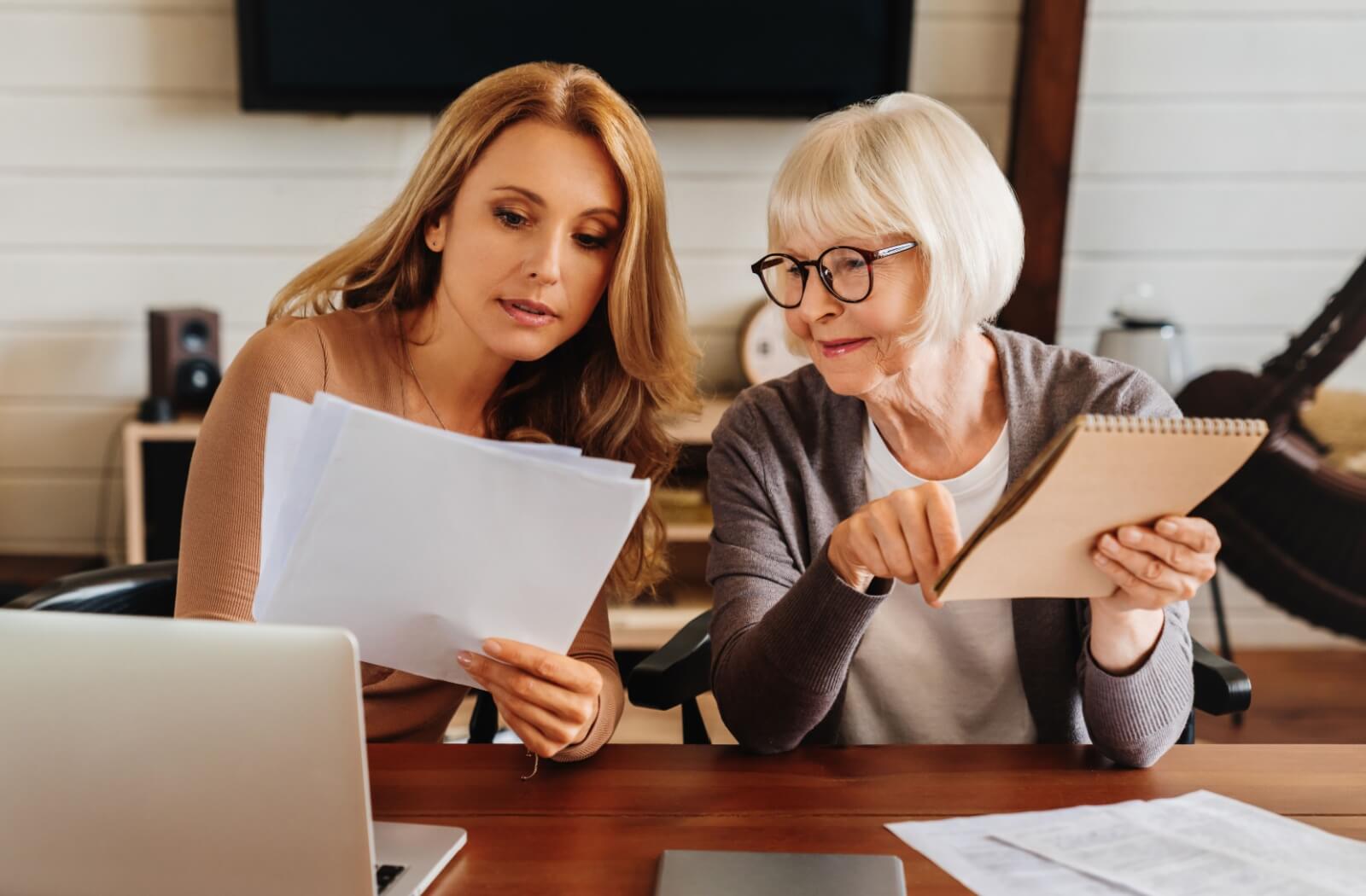 A senior parent and adult child sitting together at a kitchen table sorting financial concerns relating to memory care