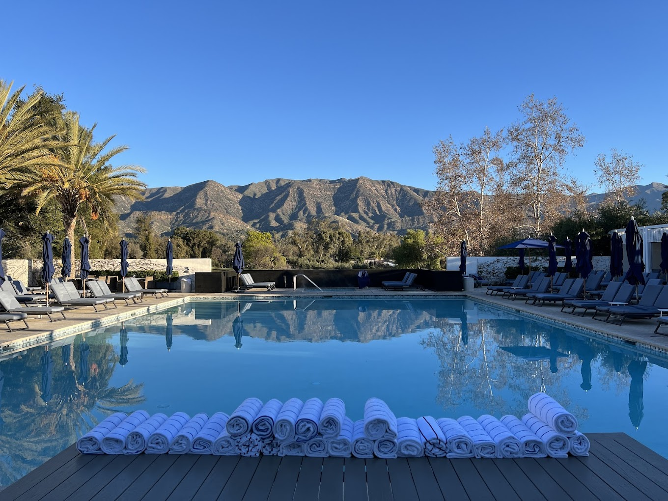 A serene poolside setting with neatly stacked towels, surrounded by lounge chairs and majestic mountain views, showcasing the luxury of ojai valley inn one of the top secret stays in California