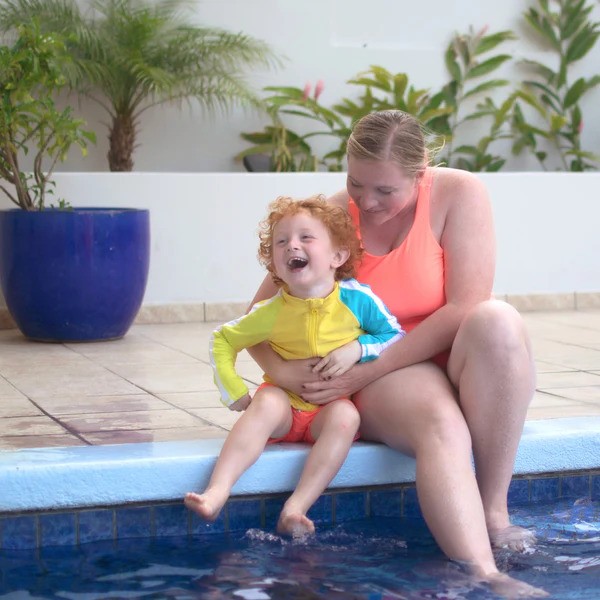 Mother and son in neon bright swimwear by SwimZip by the pool—What is the best swimsuit color for safety?