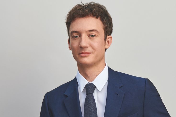 a picture of Frédéric Arnault wearing a navy color suit with white shirt and a black tie